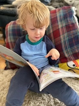 Un petit garçon aux cheveux blonds pointe une image dans son livre.