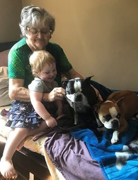 Heather porte un bébé dans ses bras en étant assises sur un lit entourée de 2 chiens