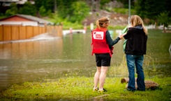 Une femme portant une veste de la Croix-Rouge réconforte une femme portant une veste noire devant une rue inondée