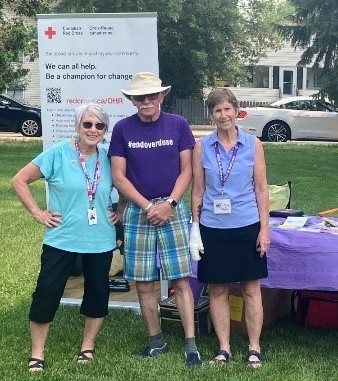 Trois personnes se tiennent devant une affiche de la Croix-Rouge canadienne.