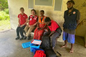 Quatre membres du personnel de la Croix-Rouge sont assis sur un banc devant des fournitures nécessaires à la distribution d’aide