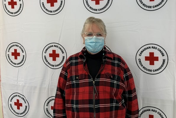 Barb portant des lunettes, un masque médical et une chemise à carreaux, se tenant devant le logo de la Croix-Rouge canadienne