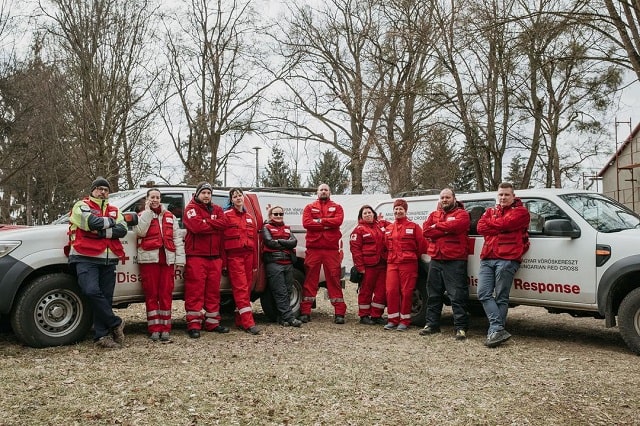 Une rangée de membres de l'équipe de la Croix-Rouge alignés devant deux véhicules de la Croix-Rouge.