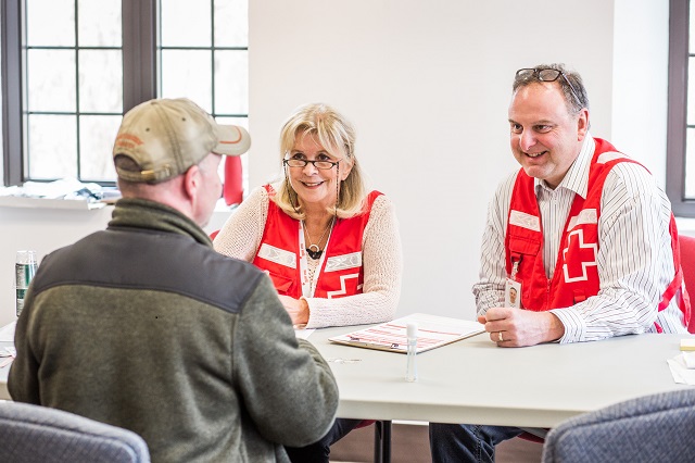 Deux bénévoles de la Croix-Rouge parlant à un homme plus âgé à une table