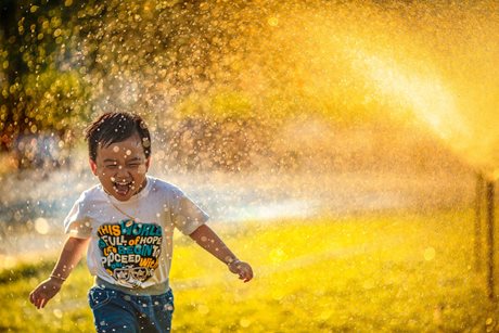 Jeune garçon avec le sourire qui court sous une fontaine d'eau