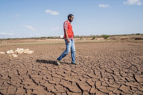 Un homme portant un gilet de la Croix-Rouge traverse un champ sec et aride.