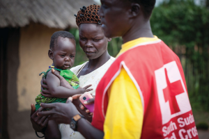 Une femme tient un bébé alors qu'un employé de la Croix-Rouge du Sud-Soudan passe à côté.