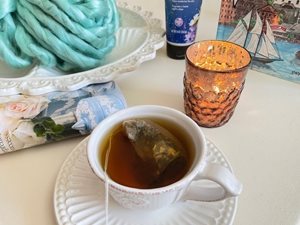 Une tasse de thé, une chandelle et de la laine bleue reposent sur une table.