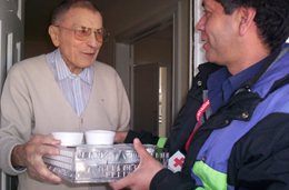 Un bénévole de la Croix-Rouge canadienne livre en main propre des denrées alimentaires emballées à une personne âgée, à sa porte.