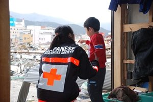 Une bénévole de la Croix-Rouge japonaise parle avec un jeune enfant devant une fenêtre.