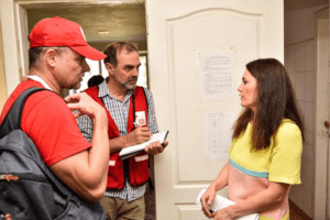 Two people wearing Red Cross apparel engage in conversation with an individual.