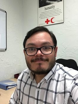 Juan, vêtu d'une chemise, de lunettes et souriant, est assis à son bureau de travail
