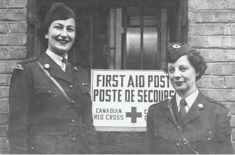 Deux femmes de la Croix-Rouge devant une afifche de poste de secours
