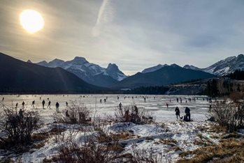 Plusieurs personnes qui sont sur un lac gelé, avec un paysage enneigé et des montagnes en arrière-plan