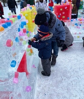 Une femme et un enfant, tous les deux habillés avec un habit d'hiver, qui jouent avec des sculptures de glace colorées