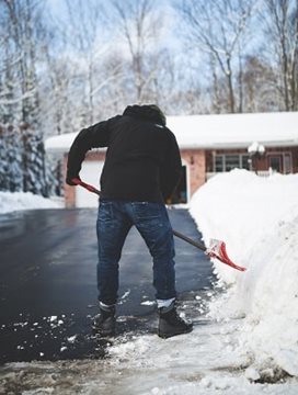 Un homme, portant un manteau d'hiver noir, qui est en train de pelleter de la neige avec une pelle rouge