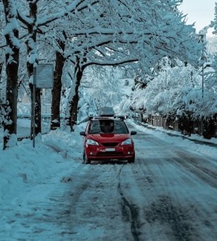 Une voiture rouge qui roule sur une route glacée, avec un paysage enneigé