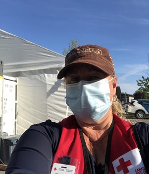 Une femme portant une casquette et un masque prend un selfie avec une tente blanche et un ciel bleu derrière elle