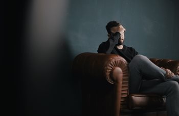 Un homme est assis sur un divan avec la main au front et semble déprimé