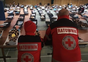 Deux hommes portant des vestes du Mouvement de la Croix-Rouge font face à un centre d'hébergement d'urgence