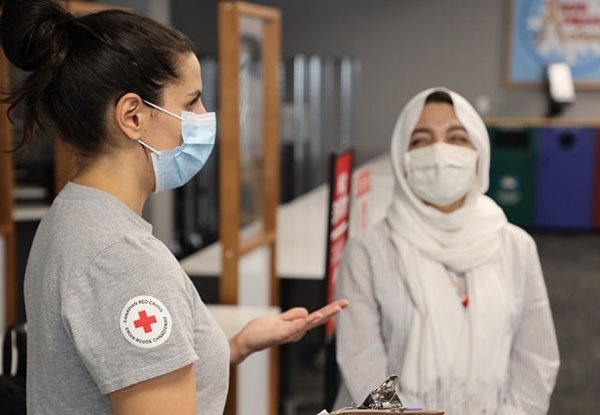 Deux femmes masquées, l'une portant un chandail de la Croix-Rouge canadienne, discutent entre elles.