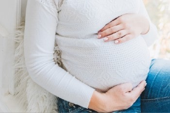 Une femme enceinte assise avec ses mains sur son ventre.