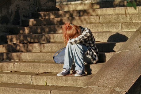 Une adolescent aux cheveux roux est assise dans des escaliers, la tête sur les genoux
