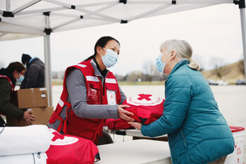Une femme portant  une veste de la Croix-Rouge offre une couverture à une dame habillée avec un manteau bleu