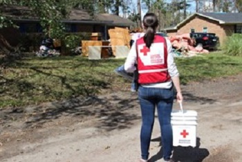 Une employée de la Croix-Rouge tient une trousse de nettoyage inondation devant une maison détruite