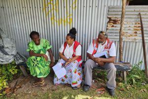 Deux membres du personnel de la Croix-Rouge sont assis à l’extérieur et discutent avec une femme.