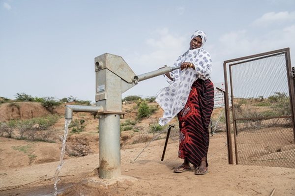 Une femme debout près d'un puits d'eau dans un champ aride.