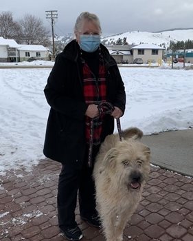 Barb, portant un manteau noire et un masque médical, avec un gros chien blanc par une laisse