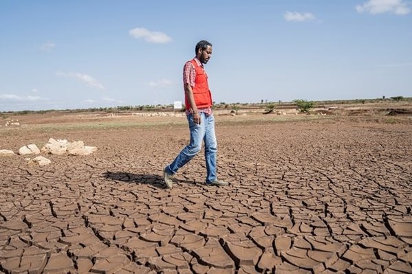 Un homme portant un gilet de la Croix-Rouge traverse un champ sec et aride.