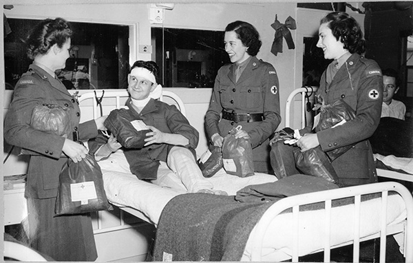 Three CRCC Welfare Officers visit a convalescing soldier overseas (ca. 1943-45) while distributing “ditty bags” on a hospital ward.-FR