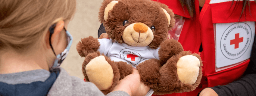 Un volontaire de la Croix-Rouge offre un ours en peluche à un petit enfant pour le réconforter.