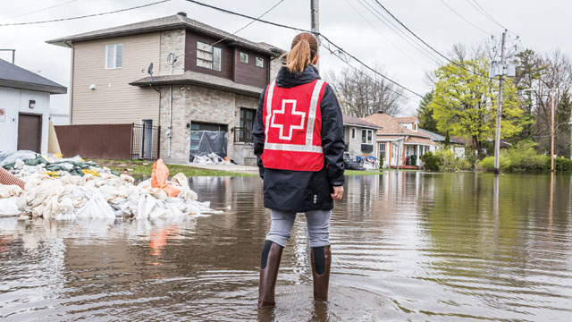 Un représentant de la Croix-Rouge portant un gilet rouge surveille l'inondation d'une rue rurale dans un quartier.