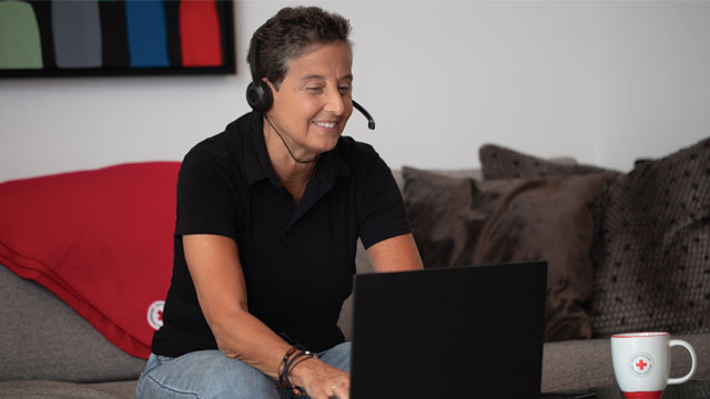 Une personne travaillant virtuellement depuis son canapé, portant un casque et semblant communiquer via son ordinateur portable.
