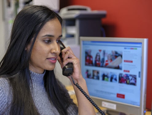 Femme répond au téléphone, avec le site Web de la Croix-Rouge canadienne sur son écran d'ordinateur.