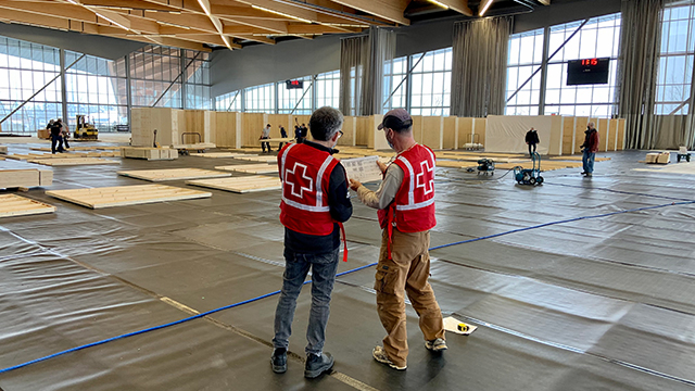 Deux hommes de la Croix-Rouge canadienne examinent les plans des bâtiments à l'intérieur d'un centre