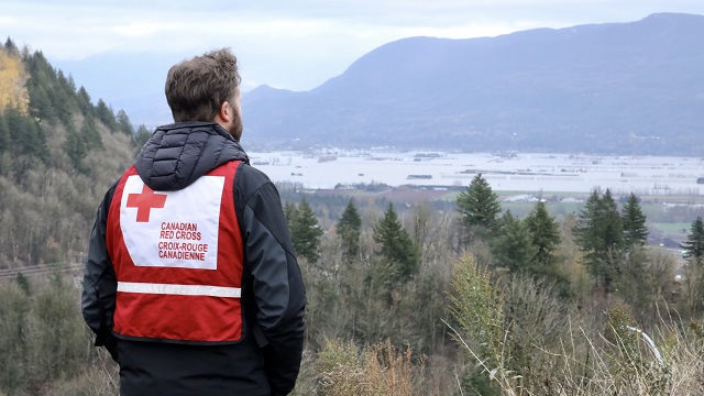 Man in Red Cross vest staring at the floods in BC