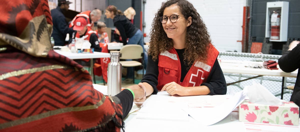 Une employée de la Croix-Rouge sourit tandis qu'elle s'assoit avec un bénéficiaire et examine des documents.