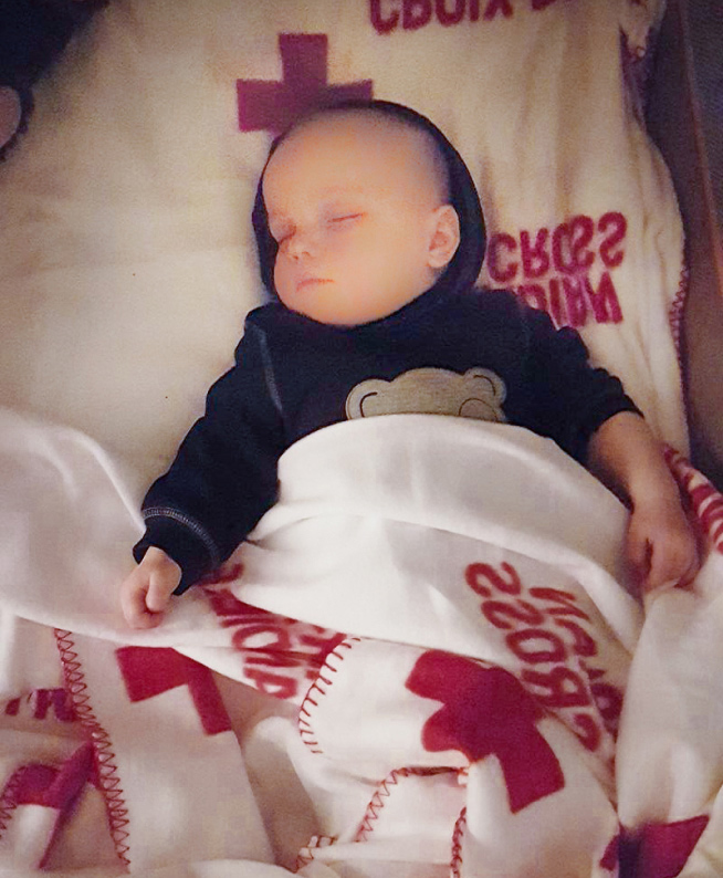 Un bébé endormi est confortablement allongé, blotti sous une couverture Rec Cross.