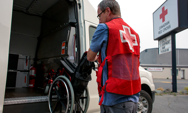 Un employé de la Croix-Rouge canadienne livrant un fauteuil roulant le charge dans une camionnette.