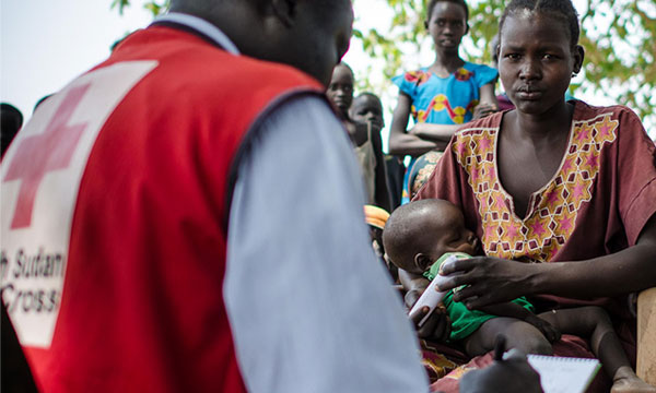 Un volontaire de la Croix-Rouge soudanaise prend des notes sur un bloc-notes, tandis qu'une mère tient son bébé.