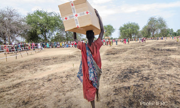 Une personne porte une grande boîte remplie d'aide de la Croix-Rouge au-dessus de sa tête, photo de la IFRC.