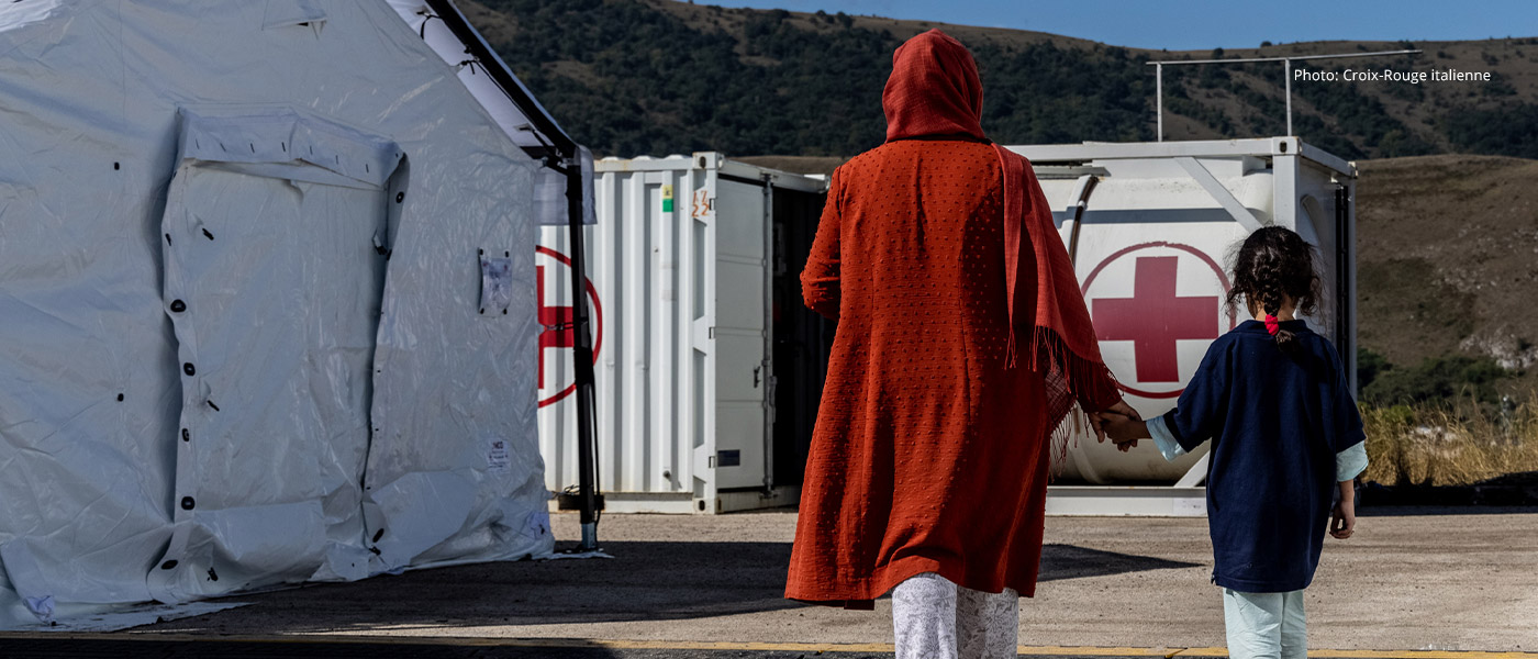 Une femme tient la main d'un enfant, marchant entre des tentes d'urgence.