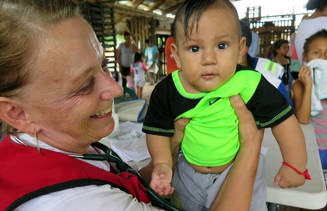 Une travailleuse humanitaire de la Croix-Rouge canadienne tient dans ses bras un jeune garçon examiné à la clinique de santé mobile. 