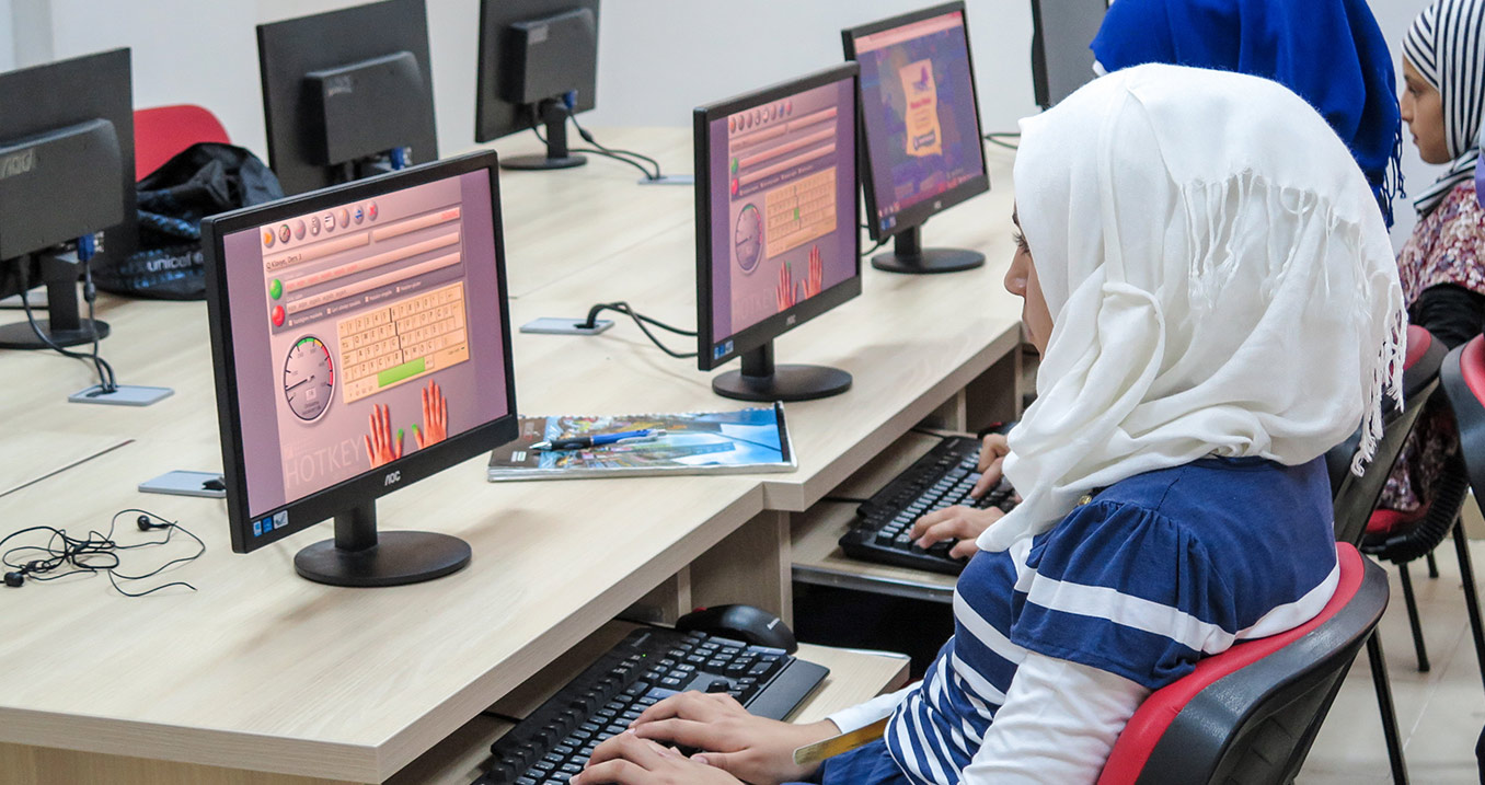 Une femme portant un hijab blanc se concentre sur son écran d'ordinateur.