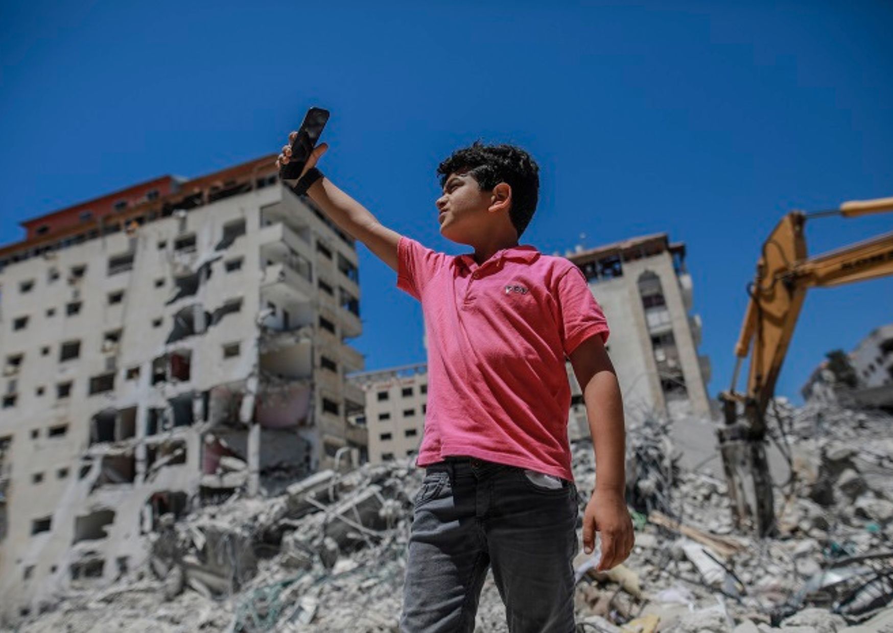 Un jeune garçon dans une zone de guerre se tient sur un tas de décombres.
