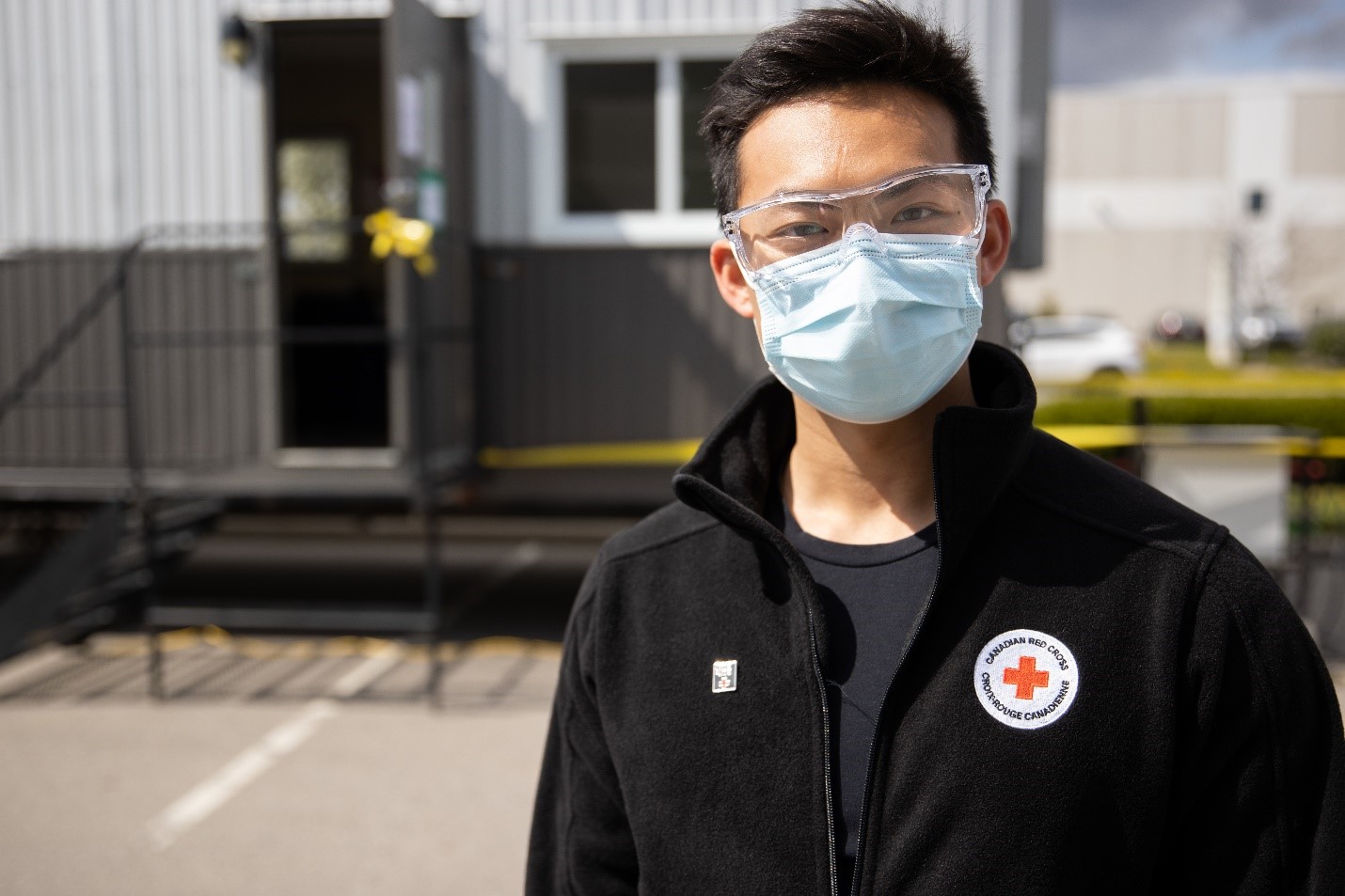 Un travailleur de la Croix-Rouge à l’extérieur portant un masque médical et des lunettes de protection